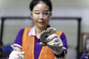 Closeup hands of Asian woman industrial engineer hold and looking example small gear to working designing mechanical parts engineering at industrial workshop. photo