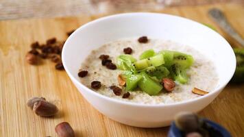 cooked oatmeal with kiwi, honey and nuts in a bowl on a wooden table video