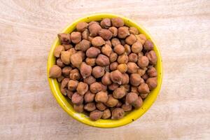 Flat Lay of Black or Brown Chickpeas in a Yellow Bowl on Neutral Wooden Background photo