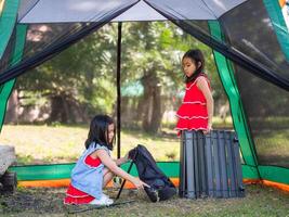 Two sisters are helping each other set up a table in nature on a sunny day. Family camping in the woods on summer vacation photo