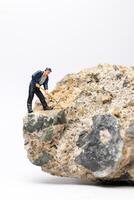 Miniature worker using a pickaxe to chip away at a large rock on white background photo