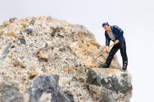 Miniature worker using a pickaxe to chip away at a large rock photo