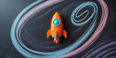 orange toy space rocket and stars on black chalkboard with galaxy drawn with chalk with copy space on right photo