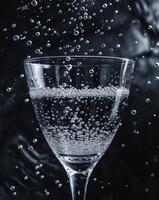 Clear Glass of Sparkling Water with Bubbles on Dark Background photo