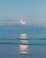Serene cloud reflection over tranquil ocean with crescent moon at dusk photo