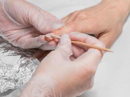 Manicurist removes the base coat from the nail with an orange stick during the manicure procedure at the Spa. photo