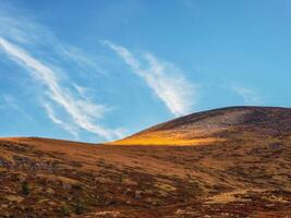 Minimalistic beautiful mountain scenery with golden light on slopes mountains. Scenic mountain landscape with illuminating color in blue sky. photo