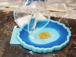 The art process of pouring epoxy resin into a golden toy. Technology process of creating a painting in style resin art, works with epoxy in studio, makes a wooden stand with the image. Close up. photo