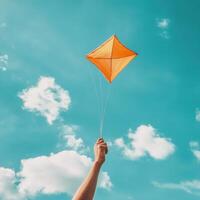 Bright orange kite soaring high against a clear blue sky with fluffy clouds on a sunny day photo