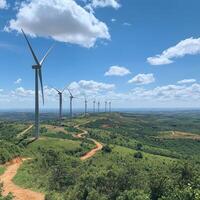 Wind turbines stand tall against a blue sky in a scenic green landscape with rolling hills and a winding dirt path photo