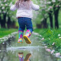 Child enjoys jumping in puddles during springtime in a blooming garden photo