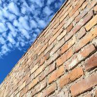 Brick wall stretches towards blue sky with scattered clouds during daylight hours photo