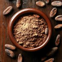 Cocoa powder in a brown bowl surrounded by cocoa beans on a wooden surface photo