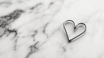 a Solitary paperclip bent into heart shape resting on white marble soft shadows and modern minimalist concept photo