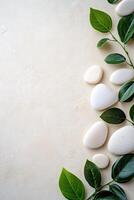 Smooth white and beige stones are arranged alongside lush green leaves on a matte beige surface, creating a serene and calming natural backdrop perfect for text overlay photo