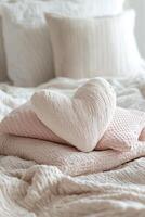 Soft bedding is neatly arranged with a heart-shaped pillow resting on textured cushions. The light color palette creates a warm and inviting atmosphere in the bedroom photo