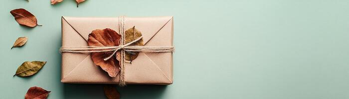 A beautifully crafted gift box made from eco-friendly recycled paper features dried autumn leaves and is neatly tied with a cotton string. The soft pastel background enhances its natural charm photo