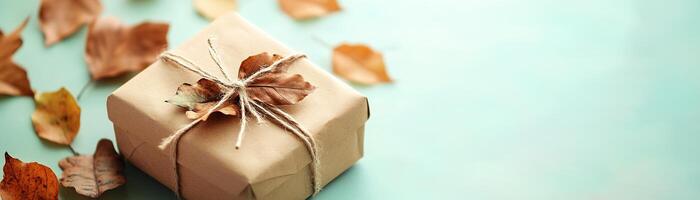 A handcrafted gift box made from recycled paper, featuring dried autumn leaves and tied with cotton string, rests on a soft pastel background, ideal for a natural gift presentation photo