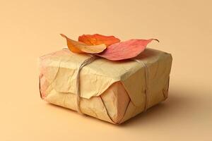 A handcrafted gift box made from recycled paper features dried autumn leaves and is tied with cotton string. It rests on a soft pastel backdrop, perfect for eco-friendly gifting photo