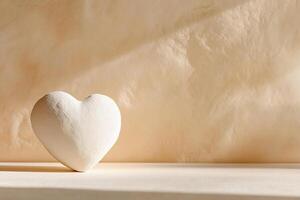 A handmade clay heart in soft white rests on a matte beige surface, creating a minimalist design. Soft shadows enhance the organic feel, offering ample space for text photo