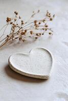 A heart-shaped plate made from light stone is elegantly set on a neutral backdrop. A delicate dried flower accentuates the calming atmosphere, perfect for stunning text overlays photo