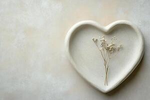 Heart-shaped plate made from light stone is placed on a smooth neutral surface. A small dried flower accent adds a touch of natural beauty, creating a calming ambiance photo
