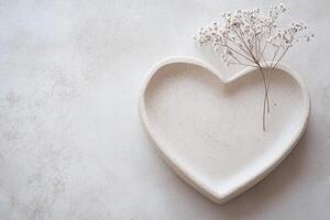 A heart-shaped plate crafted from light stone sits gracefully on a neutral surface, accented by a small dried flower. This setting creates a soothing and serene ambiance photo