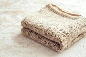 A neatly folded wool sweater in soft neutral tones rests on a smooth stone surface. The natural light enhances its cozy texture and creates a warm, inviting space photo