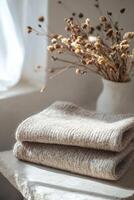 A cozy wool sweater in beige is carefully folded on a smooth stone surface. Soft natural light enhances the warm feel of the setting, highlighting the sweater's texture and inviting comfort photo