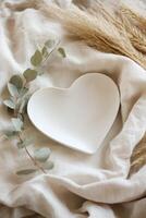 A heart-shaped plate rests on soft beige linen, accented by dried pampas grass and eucalyptus. The neutral background creates a warm, inviting space perfect for styling or decoration photo