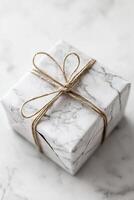 A minimalist gift box features a soft stone texture in light gray tones, elegantly tied with a thin gold string. It is placed on a clean white background, ideal for highlighting your message photo