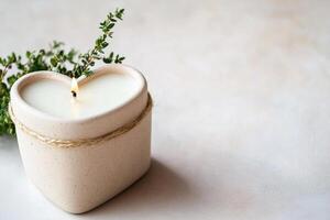 Heart-shaped soy candle in a matte recycled container, adorned with greenery, is showcased on a smooth neutral surface, ideal for eco-conscious home decor and ambiance photo