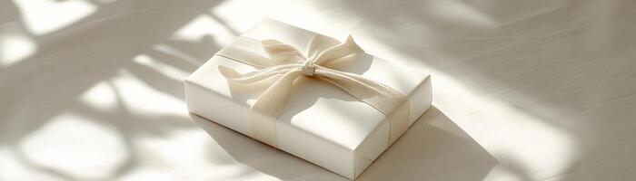 A sophisticated white matte gift box tied with a soft beige linen ribbon rests on a clean neutral surface. Soft natural shadows enhance the minimalist and elegant aesthetic, perfect for any occasion photo