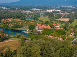 Aerial view of orange roofed buildings surrounded by greenery, small lakes, and palm trees, with mountains and urban structures in the background. photo