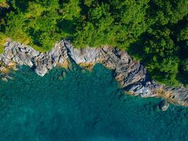 Aerial perspective of a rocky shoreline in Phuket or Phi Phi Islands, Thailand, with turquoise waters and dense green forest creating vivid contrasts. photo