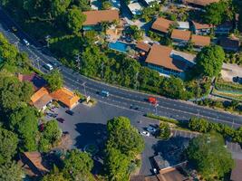 Aerial perspective of a road bordered by trees and small buildings with brown roofs in Phuket, Thailand. Vehicles and dense vegetation are visible. photo