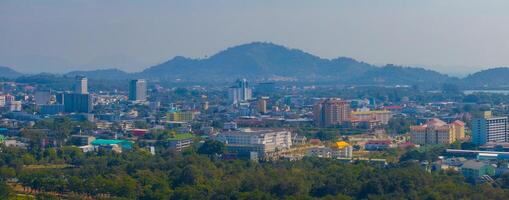 Aerial view of Phuket, Thailand, featuring modern and traditional architecture, colorful rooftops, dense greenery, and scenic rolling hills in the background. photo