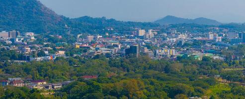Aerial view of Phuket, Thailand, featuring lush greenery, a vibrant cityscape, forested hills, and the iconic Big Buddha statue in the distance. photo