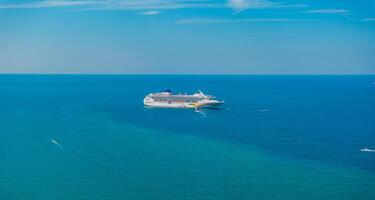 A cruise ship floats in tranquil blue waters under a clear sky, surrounded by smaller boats. No land is visible, likely near Phuket or Phi Phi Islands. photo
