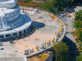 Aerial view of the Big Buddha statue in Phuket, Thailand, with golden statues, lush greenery, pathways, and nearby structures visible. photo
