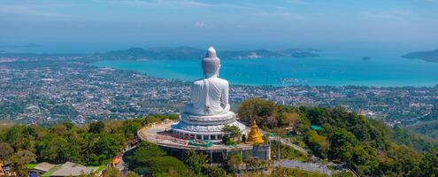 Aerial view of the Big Buddha statue in Phuket, Thailand, atop a green hill with temple structures, turquoise waters, and islands in the background. photo