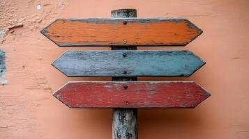 Rustic wooden direction signs in orange, red, and gray colors mounted on weathered pole, photographed against light peach background in minimalist. photo
