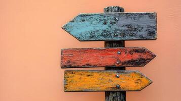 Rustic wooden direction signs in orange, red, and gray colors mounted on weathered pole, photographed light peach background in minimalist modern composition. photo