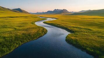Pristine meandering river flows through untouched green meadows with rolling hills and majestic mountain backdrop, captured in aerial view, showcasing vibrant spring colors. photo