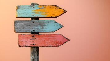 Rustic wooden direction signs in orange, red, and gray colors on weathered pole, photographed against light peach background in minimalist modern composition. photo