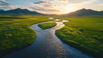 Pristine meandering river flows through untouched green meadows with rolling hills and majestic mountain backdrop, captured in aerial view during golden hour, showcasing spring. photo
