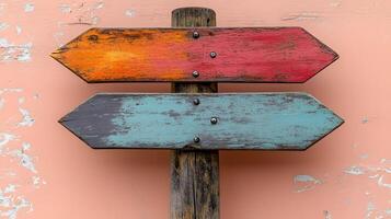 Rustic wooden direction signs in orange, red, and gray colors mounted on pole, photographed against light peach background in minimalist modern composition. photo