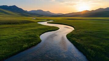 Pristine meandering river flows through untouched green meadows with rolling hills and majestic mountain backdrop, captured in aerial view during golden hour, vibrant spring. photo