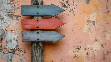 Rustic wooden direction signs in orange, red, and gray colors mounted on weathered pole, against light peach background in minimalist modern composition. photo