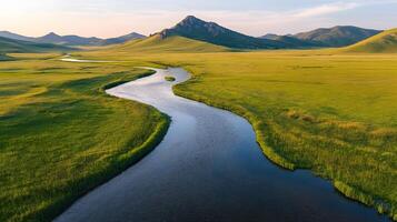 Pristine meandering river flows through untouched green meadows with rolling hills and majestic mountain backdrop, captured in aerial view during golden hour, showcasing spring colors. photo